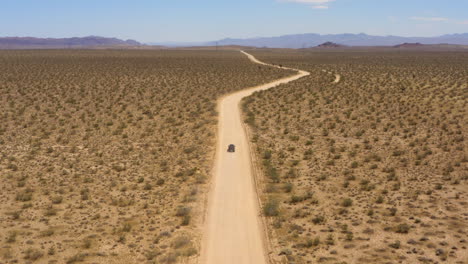 Black-SUV-approaches-a-curve-in-an-otherwise-straight-road-through-the-plains-in-the-Mojave-Desert-on-a-clear-blue-day