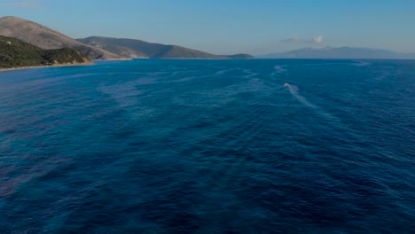 Boat-sailing-across-deep-blue-azure-sea-surrounded-by-mountains-near-Corfu-island