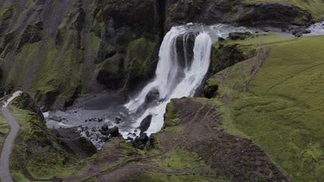 Cascada-Fagrifoss-Que-Fluye-En-Los-Acantilados-Volcánicos-Cubiertos-De-Musgo-Con-Turistas-Mirando-En-La-Plataforma-De-Observación-En-El-Sureste-De-Islandia