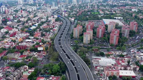 Sensational-aerial-flight-above-traffic-and-cars-traveling-downtown-Mexico-City-curvy-Periferico-Sur-expressway,-city-center,-residential-buildings-and-Mixcoac-towers,-Mexico,-overhead-drone-approach