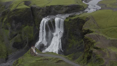 Tourists-Watching-The-Scenic-Water-Cascade-In-The-Astounding-Fagrifoss-Waterfall-In-Southeast-Iceland---aerial-drone---pullback-shot