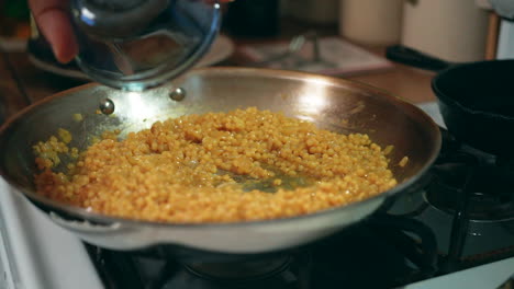 Adding-apple-cider-vinegar-to-a-pan-of-couscous-simmering-in-a-stove-top-skillet---slow-motion