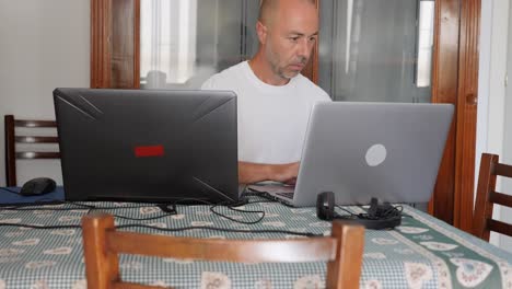 Glatzköpfiger-Mann-Mittleren-Alters,-Der-Zu-Hause-Mit-Zwei-Laptops-Arbeitet