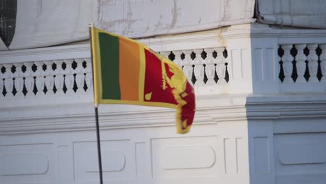 Sri-Lankan-National-Flag-in-a-pole-wave-with-the-breeze-in-front-of-the-Rampart-Hotel-and-Restaurant-in-Galle-Fort-Sunset-lighting-in-the-background,-Slow-Motion-static-b-roll-clip