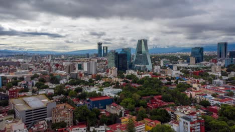 Hyperlapse:-spectacular-dramatic-downtown-Mexico-city-center-backward-flight-above-skyscrapers,-buildings,-highway,-roads,-and-Plaza-Manacar-mall-with-mountain-range-in-background-on-cloudy-day,-drone