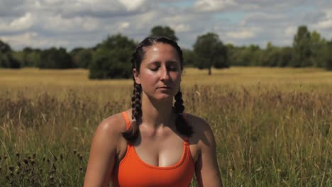 Woman-sitting-in-long-grass-field-yoga-meditating-day-time-sunny-UK,-Hertfordshire-Medium-shot-pan-left-to-right