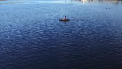 Drone-Flying-Across-The-Bay-With-A-Woman-Kayaking-In-Gig-Harbor-Marina-And-Boatyard,-Gig-Harbor,-Washington---aerial