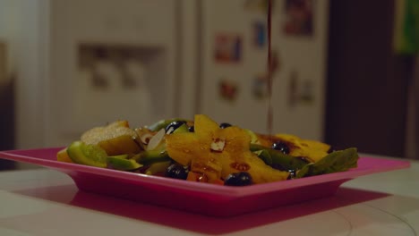 Nahaufnahme-Von-Vinaigrette-Salatdressing,-Das-In-Zeitlupe-Auf-Einen-Teller-Mit-Obstsalat-Gegossen-Wird