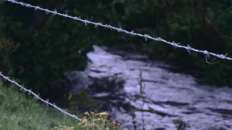 Stacheldrahtzaun-Mit-Einem-Fluss,-Der-Im-Hintergrund-In-Der-Landschaft-Nordirlands-Fließt