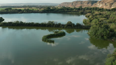 Drone-shot-of-Spanish-lagoon-or-lake-flying-over-trees-with-mountain-background