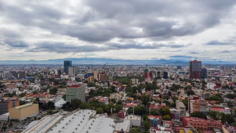 Hyperlapse:-dramatic-downtown-Mexico-city-center-Benito-Juarez-neighborhood-sideways-flight-above-skyscrapers,-buildings,-highway,-and-roads-with-mountain-range-in-background-on-cloudy-day,-drone