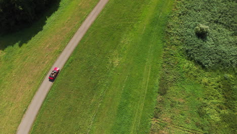 Top-Down-View-Of-A-Red-Convertible-Car-Driving-On-The-Road-Surrounded-By-The-Lush-Green-Meadow-And-Field-On-A-Sunny-Day-In-Zwolle,-Netherlands