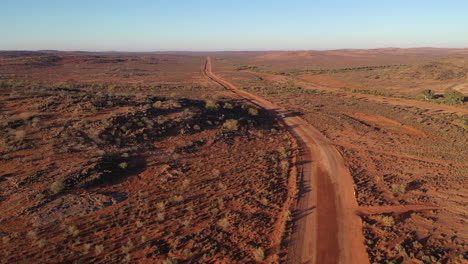 Aerial:-Drone-shot-tracking-a-vehicle-driving-down-an-empty-road-in-the-Australian-outback-towards-the-horizon-near-Broken-Hill,-Australia