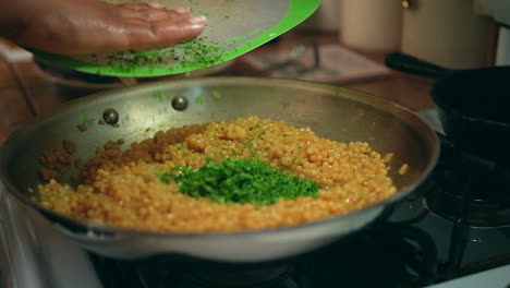Adding-chopped-basil-and-bacon-to-a-sizzling-skillet-of-couscous-on-the-stove-in-slow-motion