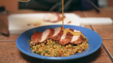 Drizzling-gravy-on-a-plate-of-fried-chicken-breast-on-couscous-in-slow-motion