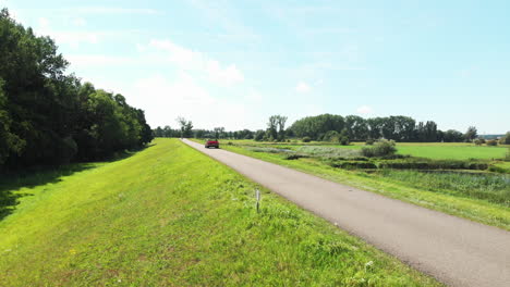Coche-Convertible-Rojo-Que-Viaja-Por-La-Carretera-Rural-En-Un-Día-Soleado-De-Verano-En-Zwolle,-Países-Bajos