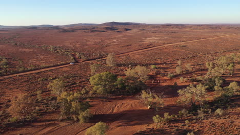 Luftaufnahme:-Drohnenaufnahme,-Die-Einem-Weißen-Fahrzeug-Folgt,-Während-Es-In-Der-Ferne-Eine-Staubige-Outback-Straße-Entlang-Fährt,-Während-Es-Sich-Weiter-Entfernt,-In-Broken-Hill,-Australien