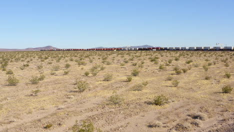 Low-view-of-two-extremely-long-freight-trains-passing-each-other-on-straight-train-tracks-in-the-desert