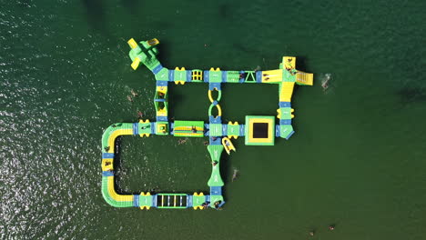 Aerial-bird-eye-shot-off-inflatable-water-games-forming-island-shape-with-kids-playing-at-the-sea