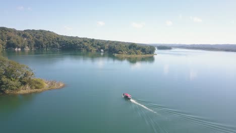 Aerial-drone-shot-of-boat-cruising-in-a-lake-to-a-jungle-in-Flores-Peten,-Guatemala