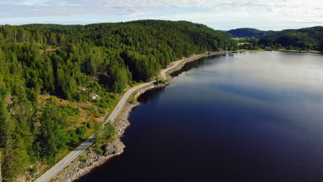 Aerial-view-of-a-road-on-the-coast-of-a-reflecting-lake,-sunny-day,-in-Sweden---dolly,-drone-shot