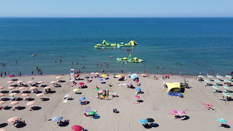 Playa-De-Arena-Con-Sombrillas-Y-Gente-Disfrutando-Del-Sol-Y-Nadando-En-El-Mar