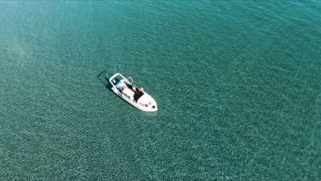 A-Small-Boat-Floating-On-The-Shallow-Clear-Water-On-A-Sunny-Weather---aerial-slowmo