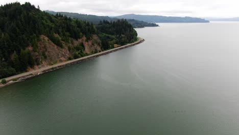 Aerial-dolly-forward-over-Columbia-River-coastline-with-car-driving-along-coastal-highway