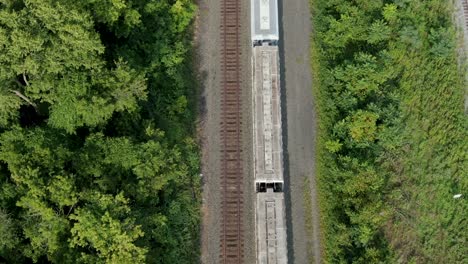 Top-down-aerial-and-tilt-reveals-stopped-train-cars-on-track,-rail-travel,-transport-concept,-drone-view,-green-grass-and-trees-in-summer-line-the-track
