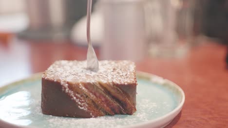 Close-up-of-a-piece-of-cake-on-a-plate-topped-with-powdered-sugar-and-a-fork