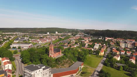 Scenic-Distant-View-Of-The-Famous-Fassberg-Church-Surrounded-By-Lush-Trees-In-The-Town-Of-Molndal,-Sweden---ascending-drone-shot