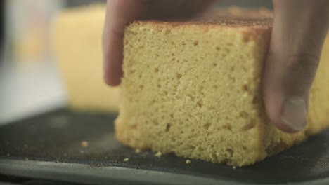A-chef-testing-the-consistency-of-a-freshly-baked-vegan-sponge-cake,-with-a-sliced-piece-of-cake-lying-in-the-focal-point