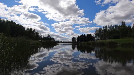 Vibrant-scenic-blue-lake-water-mirror-reflection-of-bright-clouds-and-trees-in-sky