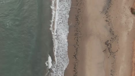 Top-View-Of-Waves-Splashing-On-The-Sandy-Shore-At-The-Beach-In-Magdalen-Islands,-Quebec,-Canada---aerial-drone
