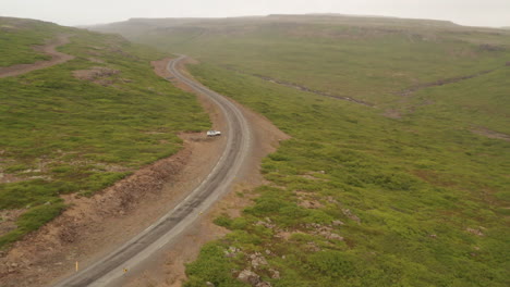 Toma-Aérea-De-Un-Automóvil-Conduciendo-Por-Un-Camino-Sinuoso-A-Través-De-Los-Desolados-Fiordos-Del-Oeste-De-Islandia