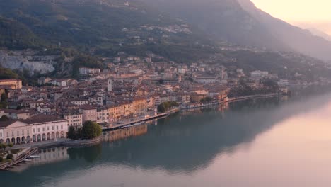 Drone-view-of-Lake-Iseo-at-sunrise,-on-the-left-the-city-of-Lovere-which-runs-along-the-lake,Bergamo-Italy
