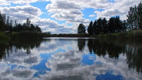 Calm-blue-lake-water-mirror-reflection-bright-scenic-cloudy-sky