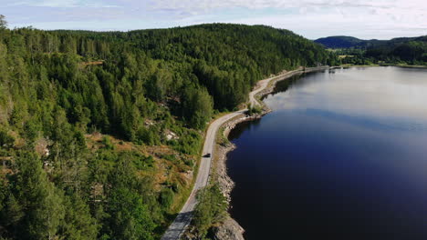 Aerial-of-car-driving-on-scenic-road-along-large-lake-in-remote-area