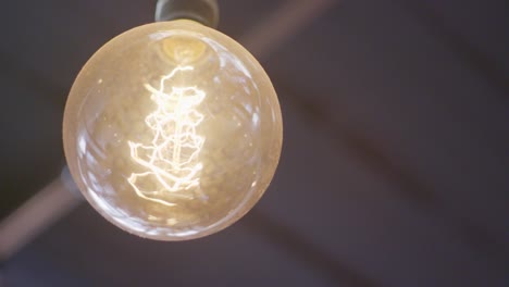 Close-up-of-a-hanging-warm-glowing-vintage-looking-light-bulb-with-a-twisted-filament-inside