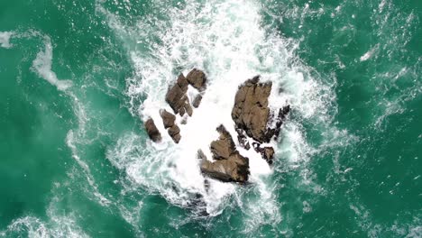 Von-Oben-Nach-Unten-Aufsteigende-Luftaufnahme-Von-Wellen,-Die-Auf-Riesige-Felsen-Im-Klaren-Ozean-In-Neuseeland-Krachen