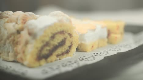 Close-up-of-swiss-roll-with-flambeed-egg-white-cream-and-powdered-sugar-on-top-with-more-cakes-in-the-background