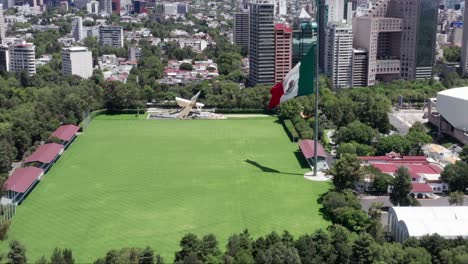 Flight-above-empty,-desolate,-deserted-and-closed-Campo-Marte-with-patriotic-Mexican-flag-waving-in-wind,-Mexico-city,-covid-19-pandemic,-lockdown-and-quarantine,-static-shot-of-overhead-aerial