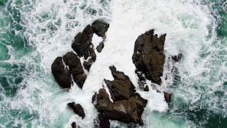 Static-aerial-top-down-of-heavy-waves-crashing-against-rock-formation-in-ocean,-Riversdale,-New-Zealand