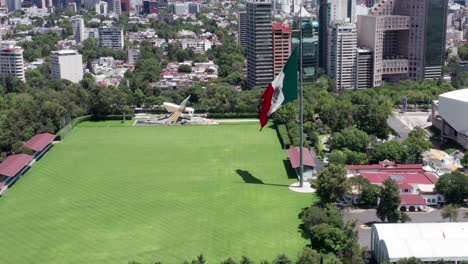 Flight-above-empty,-desolate,-deserted-and-closed-Campo-Marte-with-patriotic-Mexican-flag-waving-in-wind,-Mexico-city,-covid-19-pandemic,-lockdown-and-quarantine,-orbit-shot-of-overhead-aerial