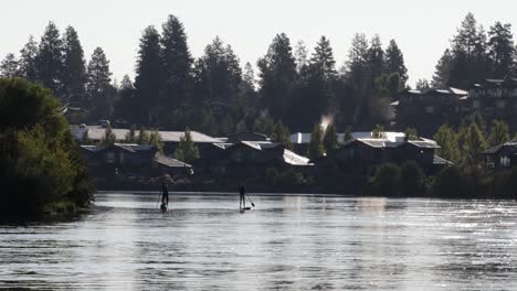 Cold-morning-river-with-two-silhouetted-paddle-boarders-and-trees