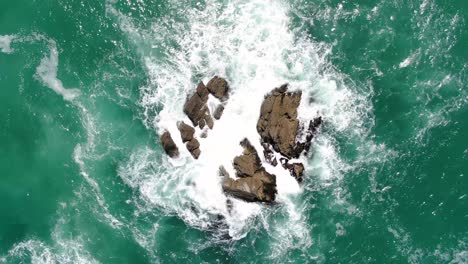 Von-Oben-Nach-Unten-Aufgenommene-Luftaufnahme-Von-Wellen,-Die-Im-Klaren-Ozean-An-Der-Küste-Neuseelands-Gegen-Riesige-Felsen-Krachen
