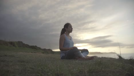 Fitness-woman-meditating-in-peacefully-atmosphere,-sunset-at-the-background,-cloudy-sky,-Asturias,-Spain,-slow-motion