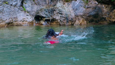 Ein-Langhaariger-Und-Dunkelhäutiger-Mann-Schwimmt-In-Türkisfarbenem-Wasser-In-Der-Nähe-Des-Wasserfalls-–-Mittlere-Aufnahme