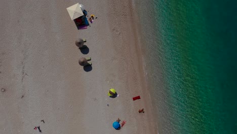 Beach-umbrellas-on-sand-washed-by-calm-clear-water-of-turquoise-sea-in-Mediterranean,-top-down-view