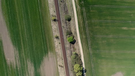 Train-track-surrounded-by-symmetrical-farmlands,-Drone-fly-over